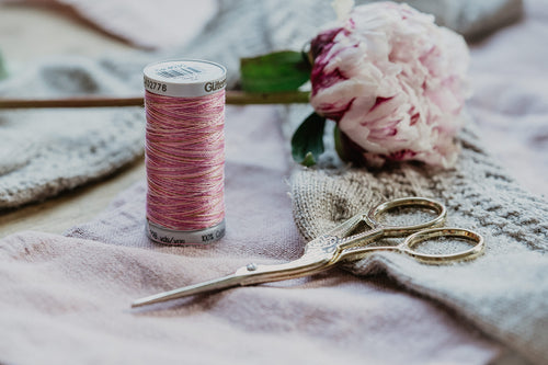 Gütermann Farbverlaufsgarn Baumwolle Rosa und eine Stickschere im Storchendesign.